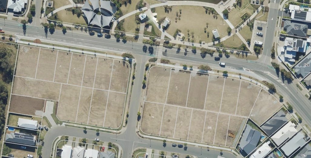 Aerial view of empty plot of land divided into multiple sections in a residential area, with roads and apartment buildings nearby.
