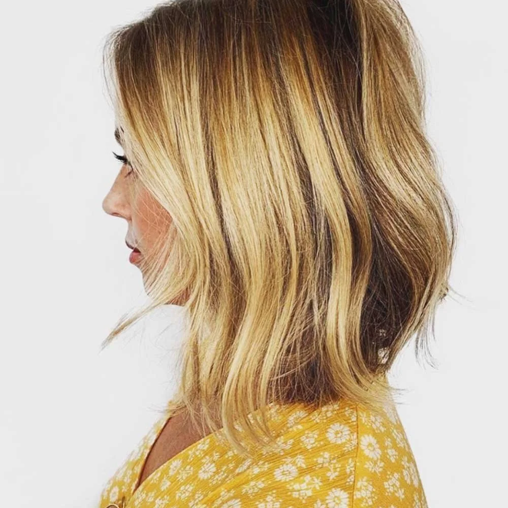 Side view of a woman with shoulder-length blonde hair and a yellow patterned top against a white background.
