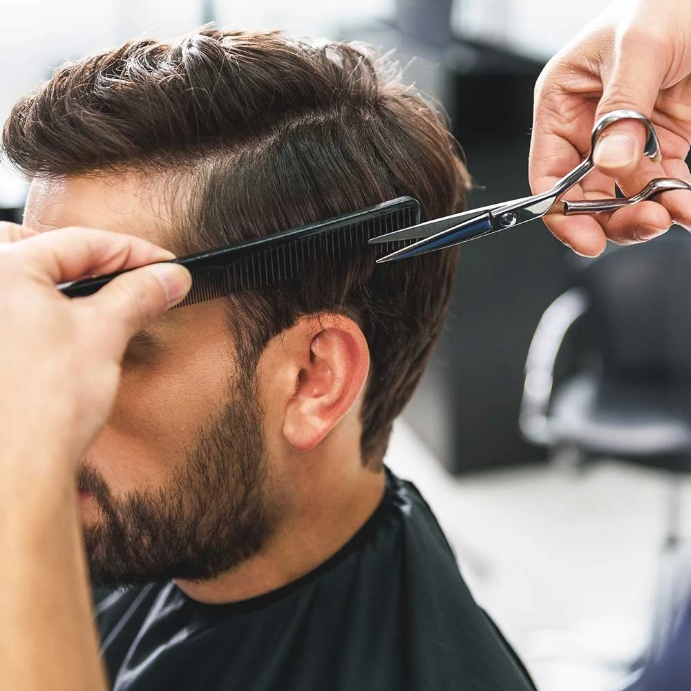 Person getting a haircut with scissors and a comb at barbershop.