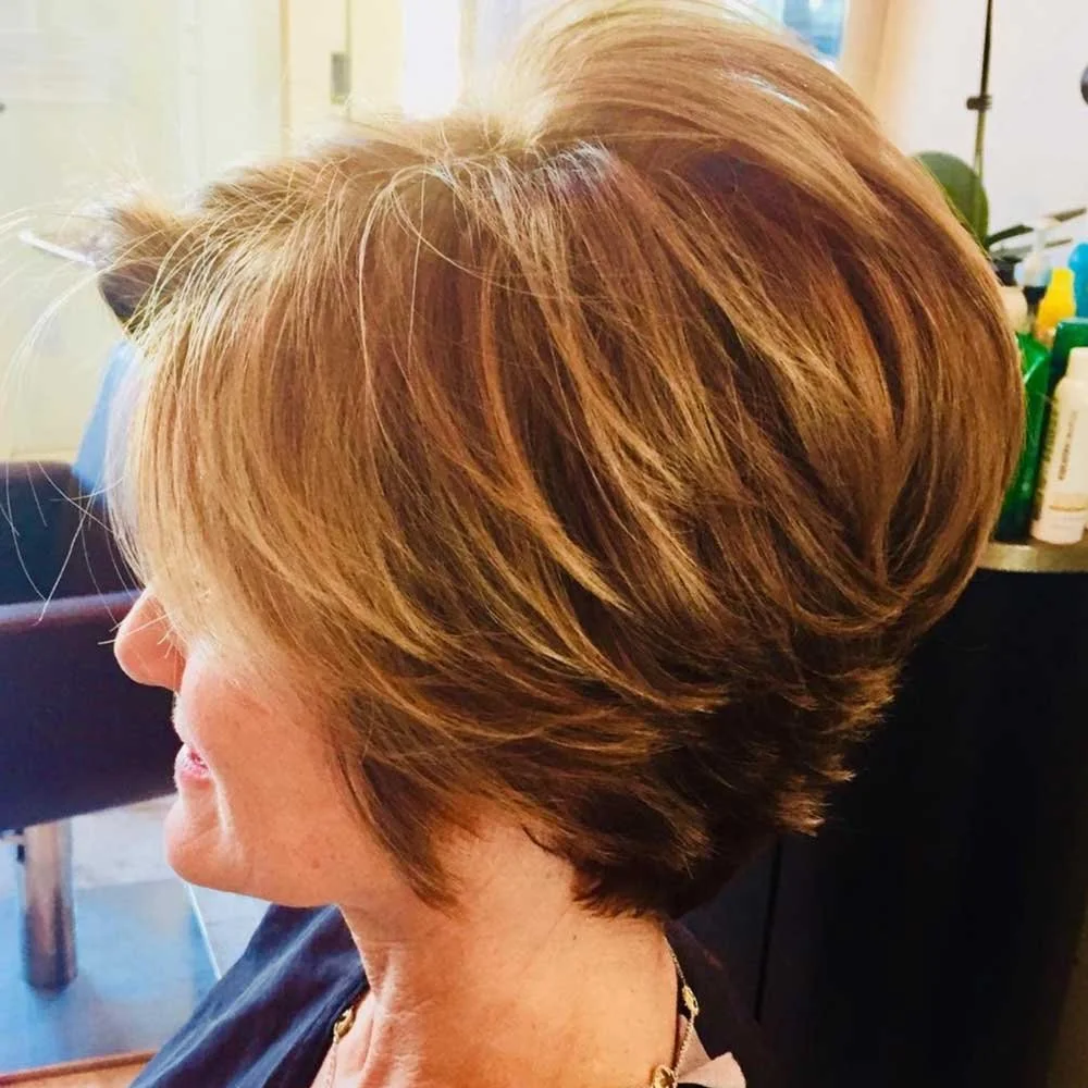 Side view of a woman with a layered, shoulder-length blonde haircut in a salon setting.