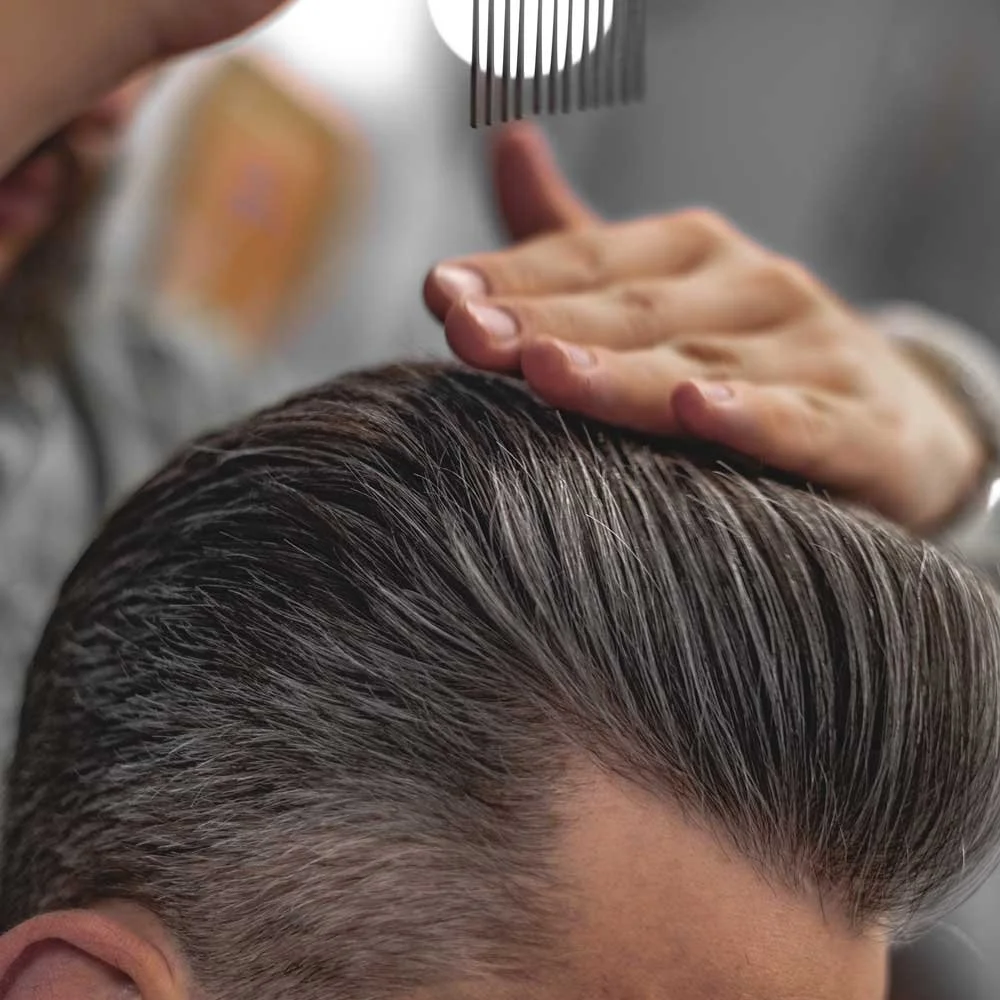 A person getting a hair treatment with a shampoo or conditioner, with a barber or stylist applying product to the scalp using a comb.