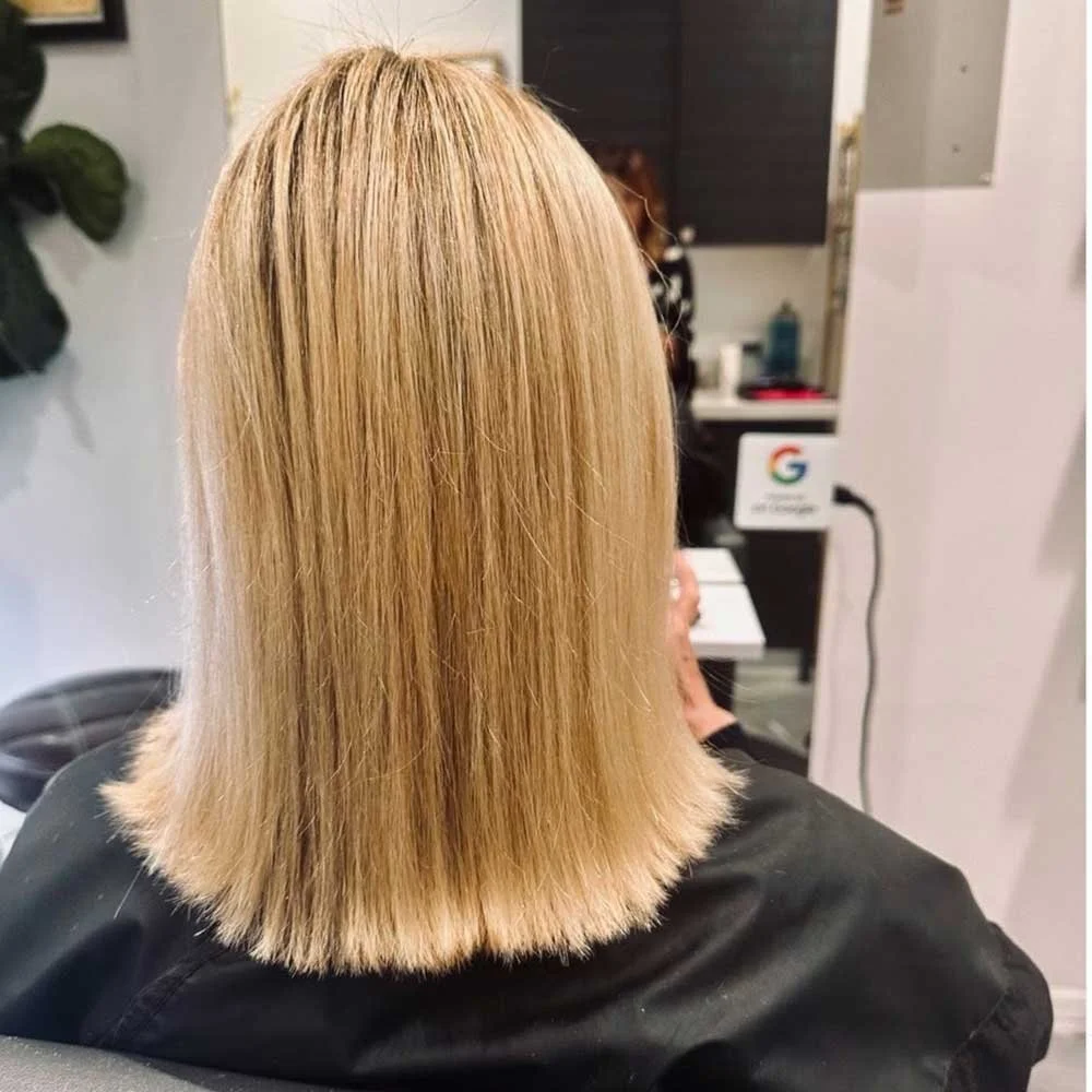 Back view of a woman with straight, shoulder-length blonde hair at a salon.