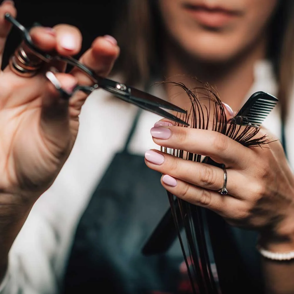 A woman getting her hair trimmed by a stylist using scissors..