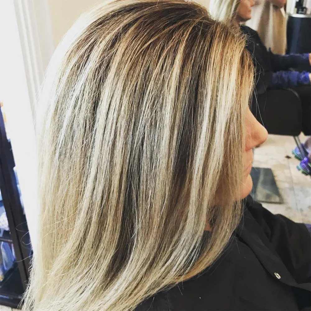 Side view of a woman with long, straight blonde hair with highlights, sitting in a salon.