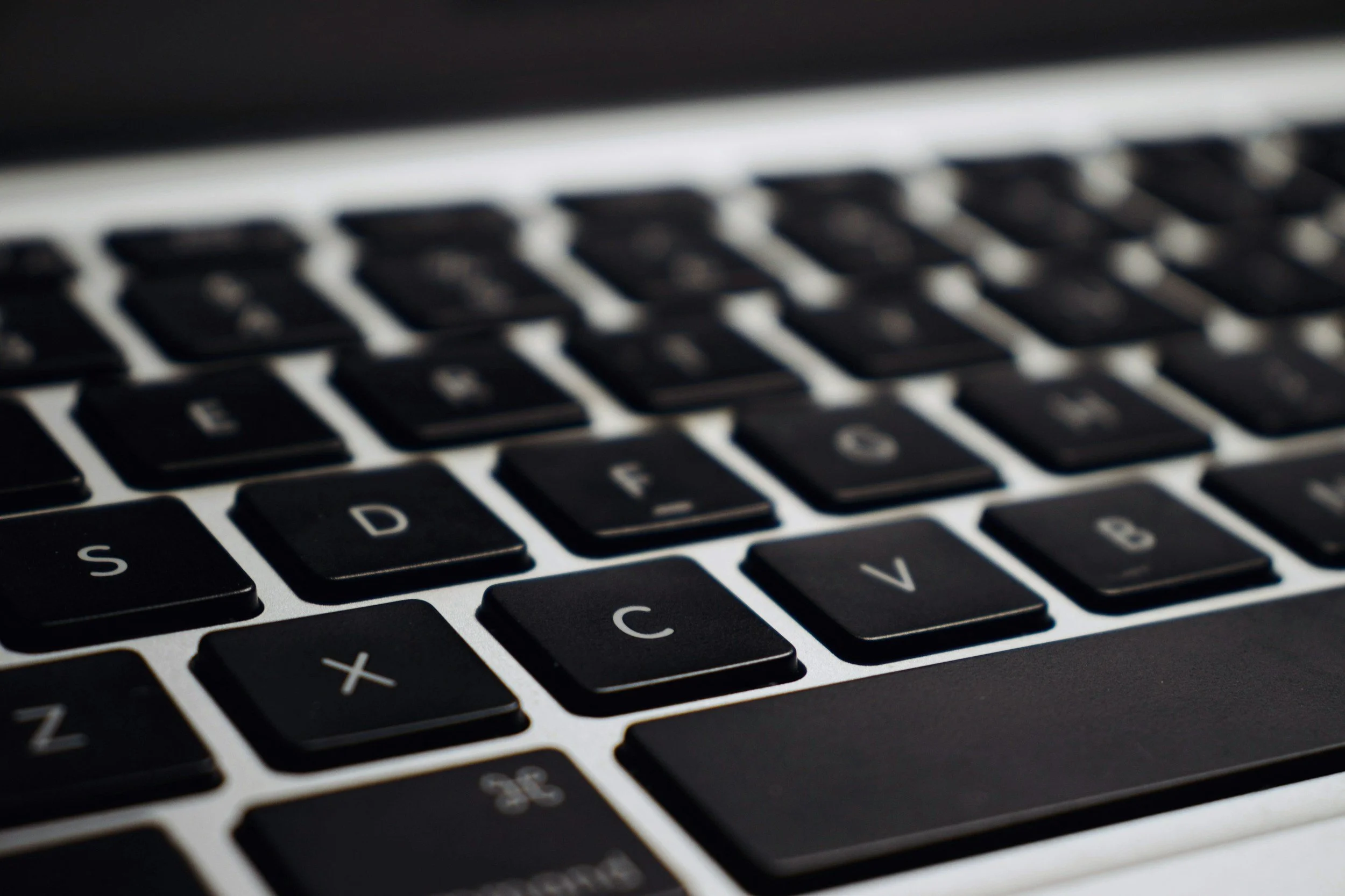 Close-up of a computer keyboard with black keys and white letters, slightly out of focus.