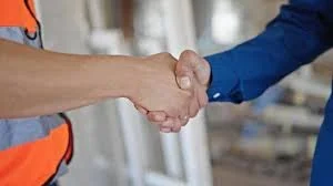 Two people shaking hands in a construction setting.