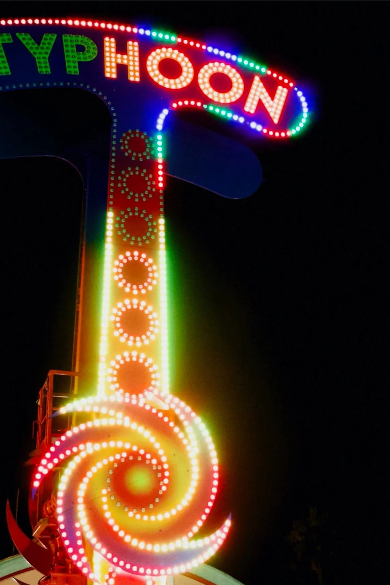 Brightly lit carnival ride sign with colorful LED lights reading 'HAPPY HOON' at night.