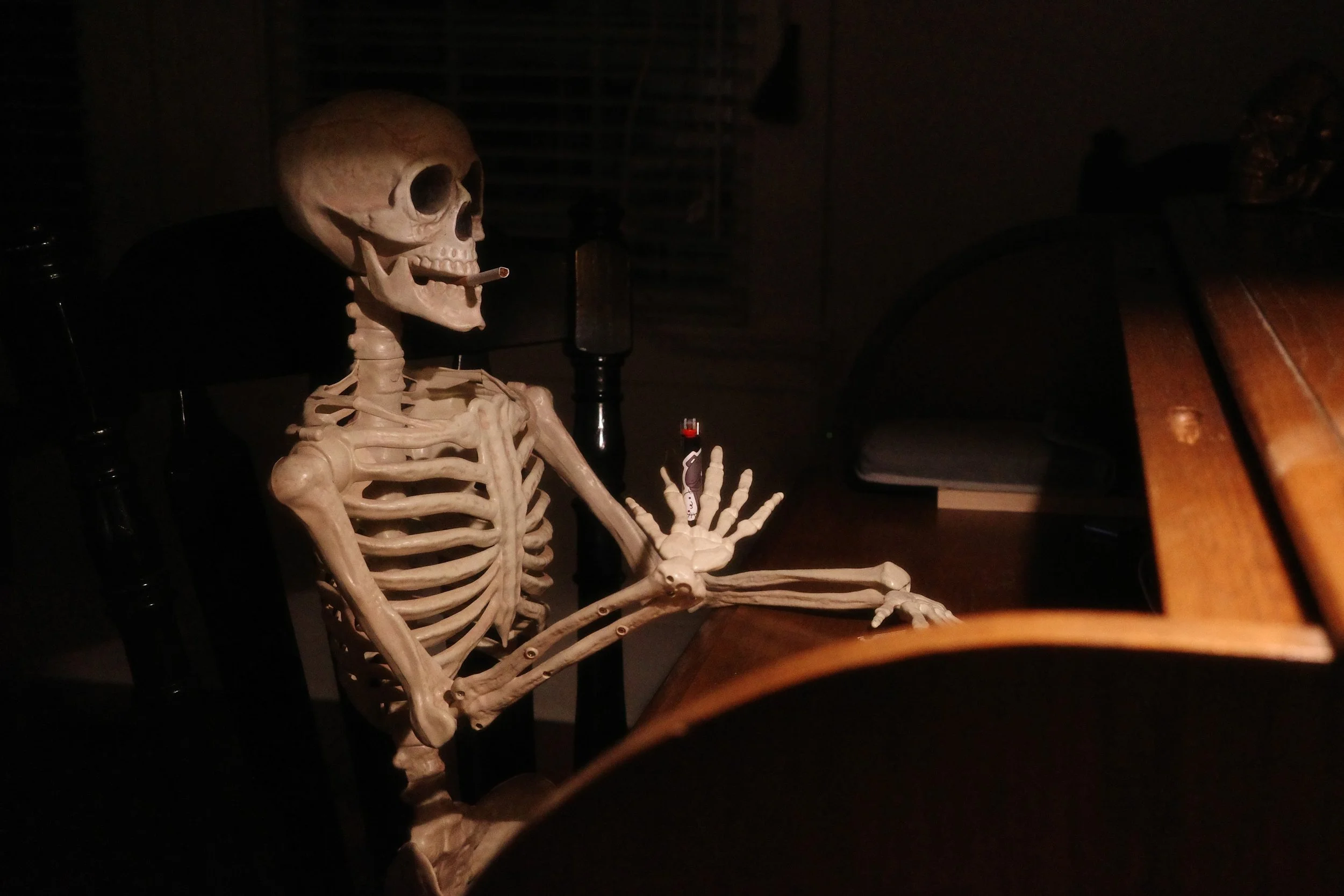 A realistic skeleton sitting at a table in a dimly lit room, preparing to light a smoke.