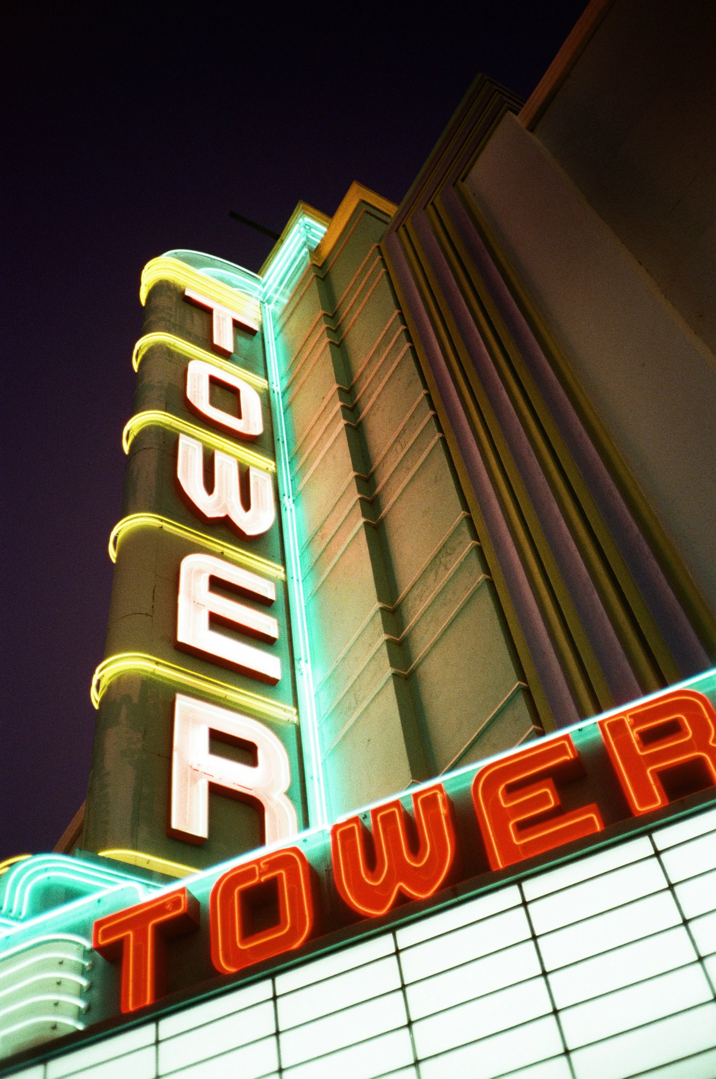 Neon sign reading 'Tower Theater' against a dark night sky, upward angle view.