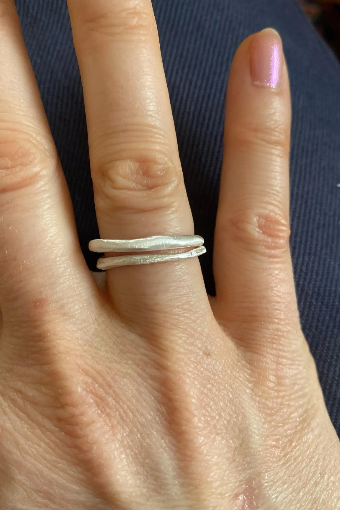 Close-up of a hand wearing a silver ring with two horizontal bands, with a pink, shiny, well-manicured fingernail.