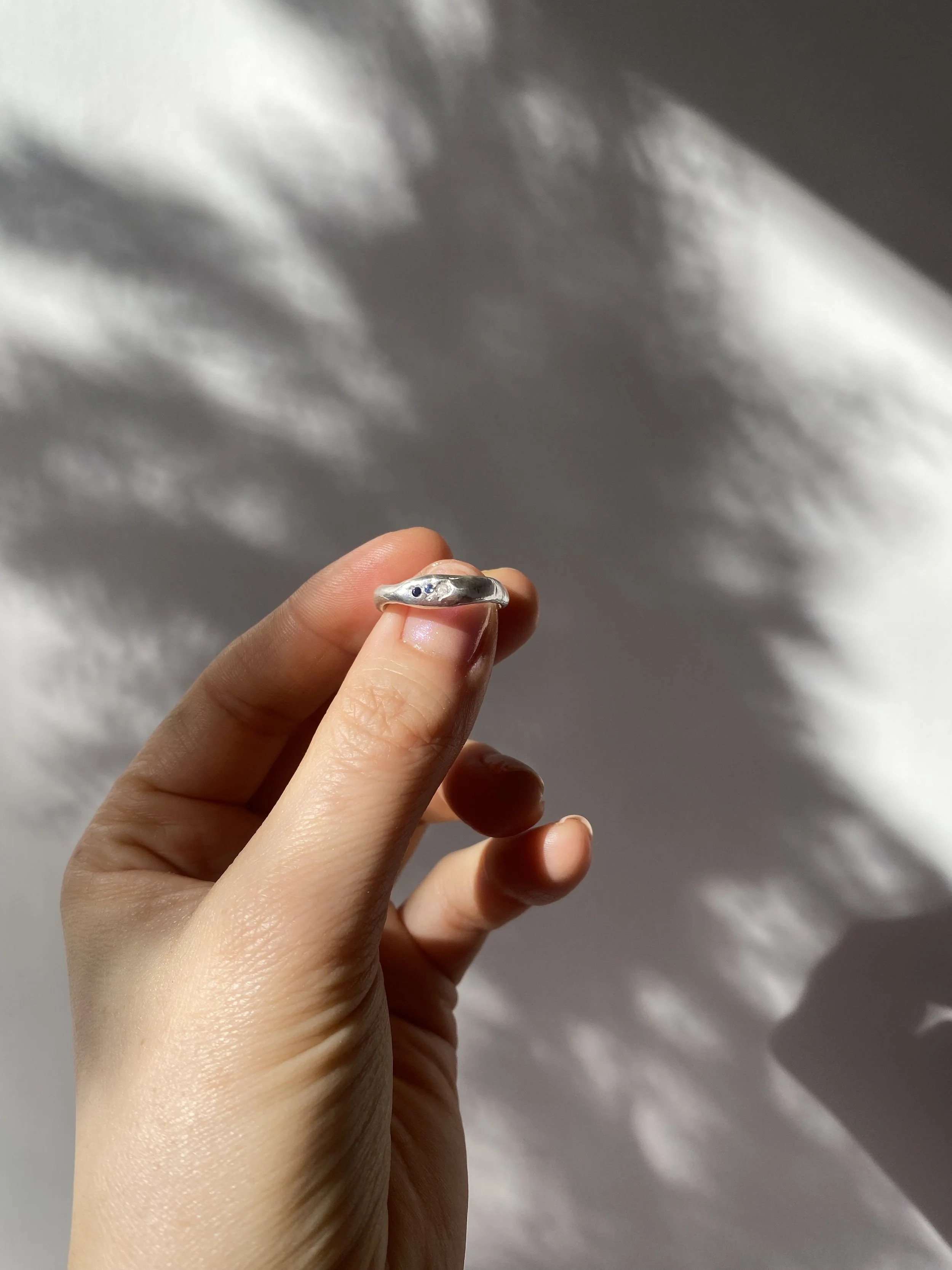 Glänzender organisch geformter Silberring mit blauen kleinen funkelnden Steinen. Der Ring ist das Ergebnis eines Silver Clay Workshops von Studio Jupiter in Hamburg.