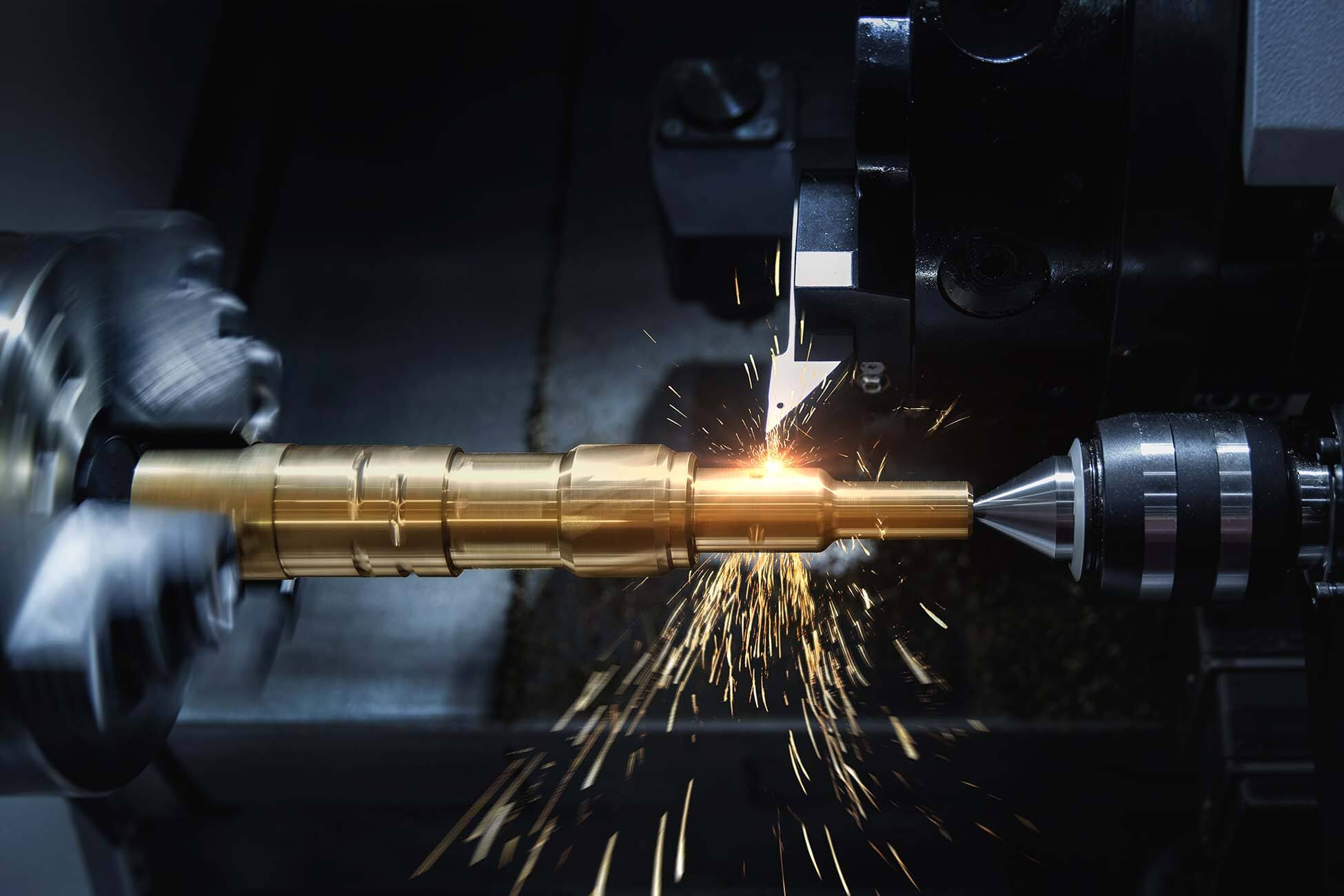A CNC machining process shaping a metallic gold-colored part with sparks flying as the cutting tool carves into the metal.