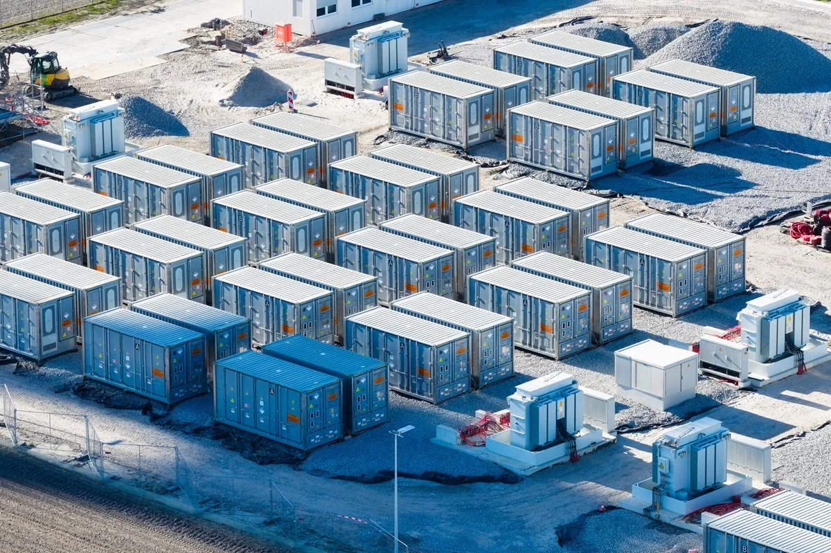 Construction site with multiple blue and white portable buildings, gravel piles, construction equipment, and fencing.