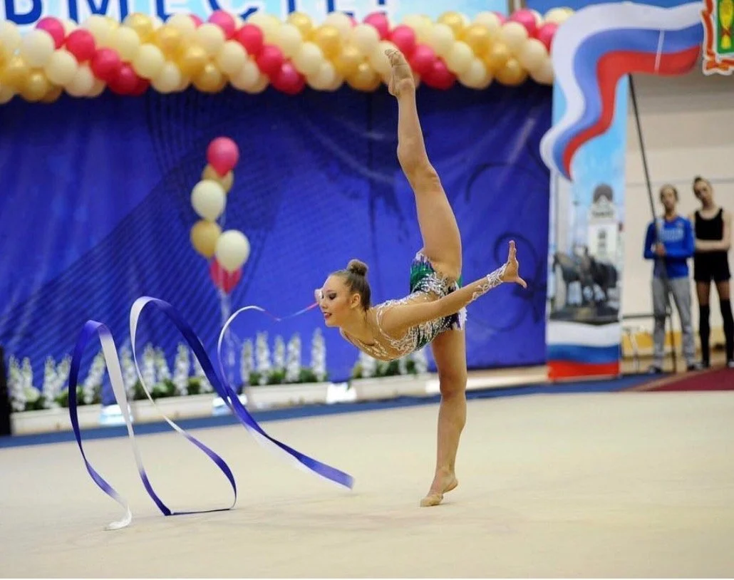 A gymnast performing a ribbon routine at a gymnastics competition, in the sports arena.