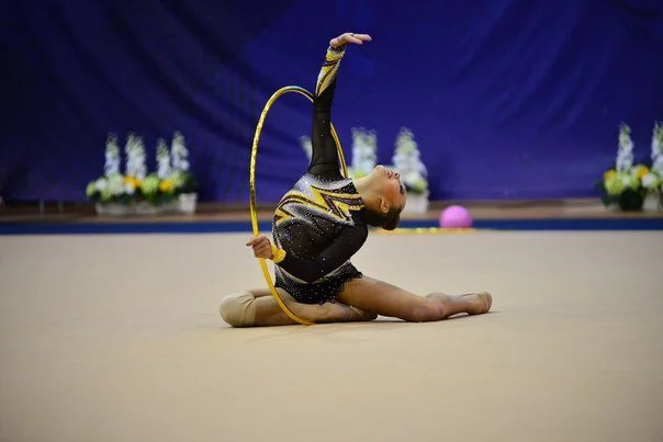 A young female gymnast performing a routine with a yellow hoop on a gymnasium floor.