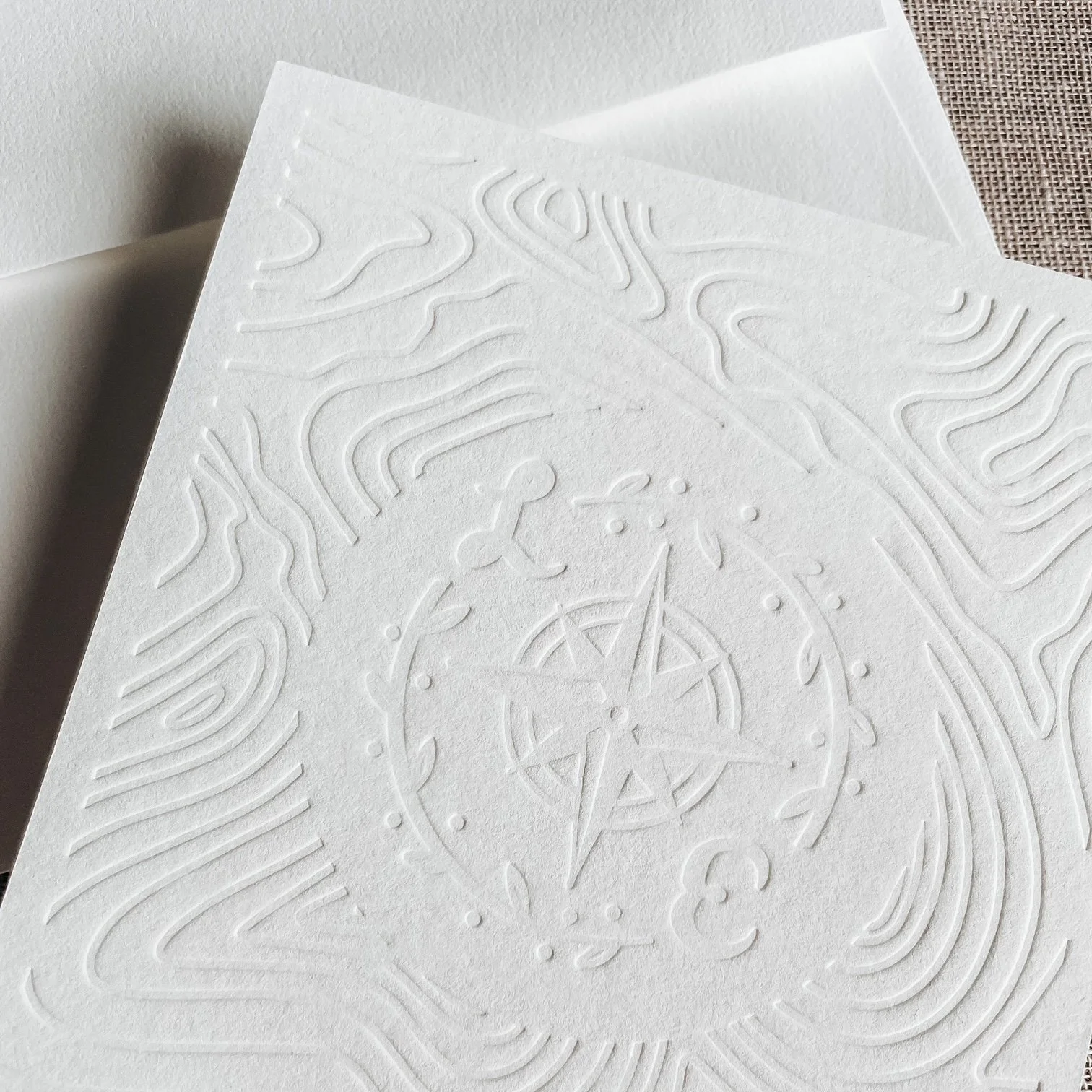 Close-up of embossed white paper with abstract and geometric patterns, including a star and lines, on a textured surface.