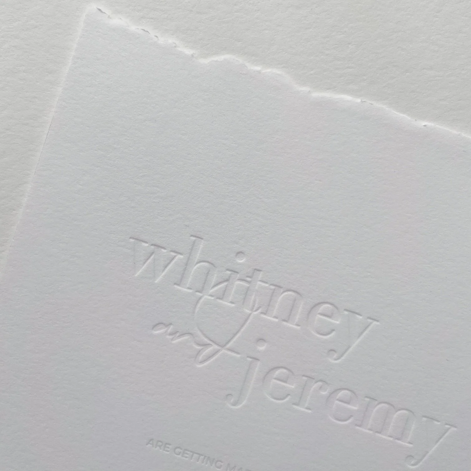 Close-up of white textured paper with embossed text and a deckled edge.