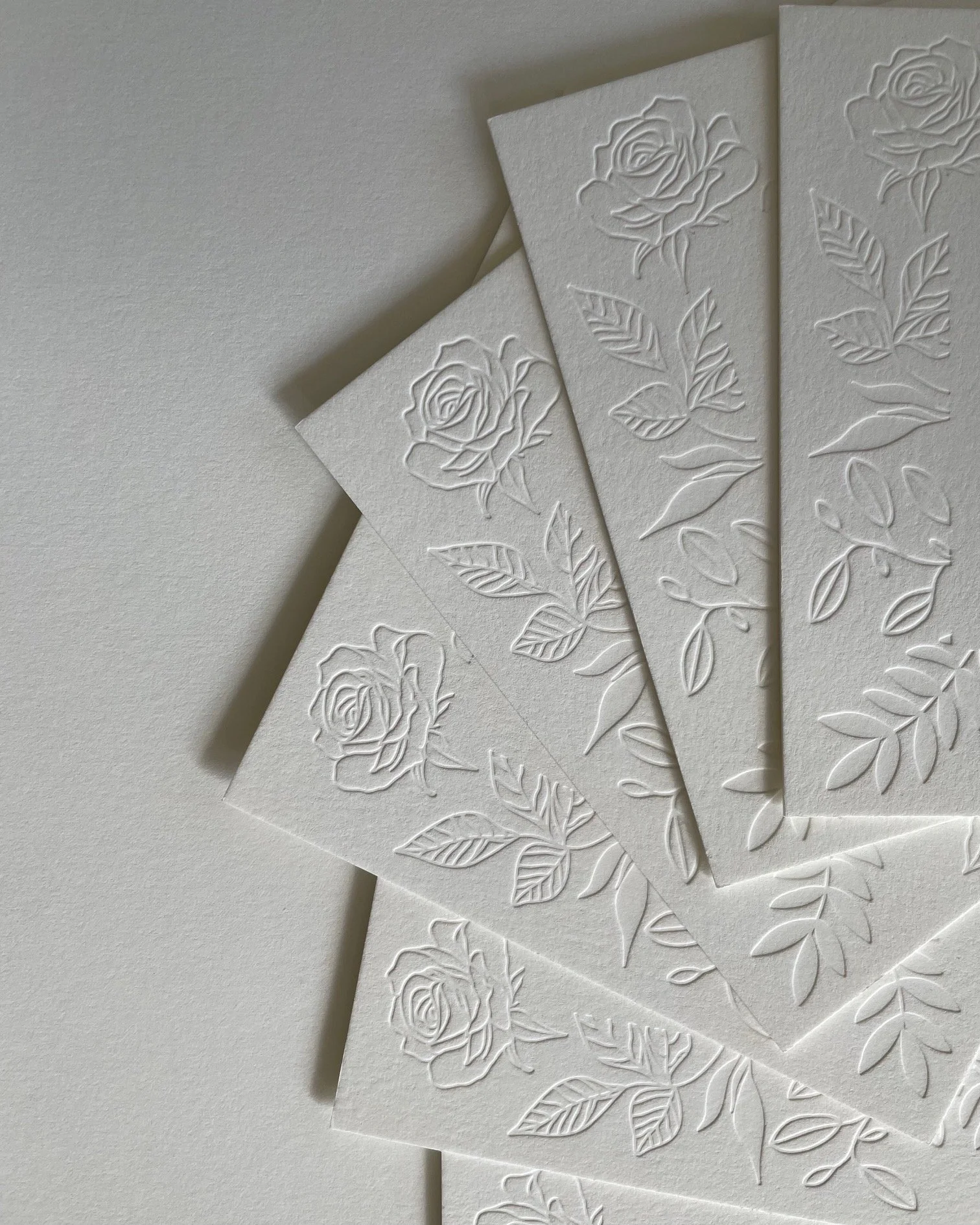 Multiple white embossed greeting cards with floral rose and leaf patterns, arranged on a white surface.