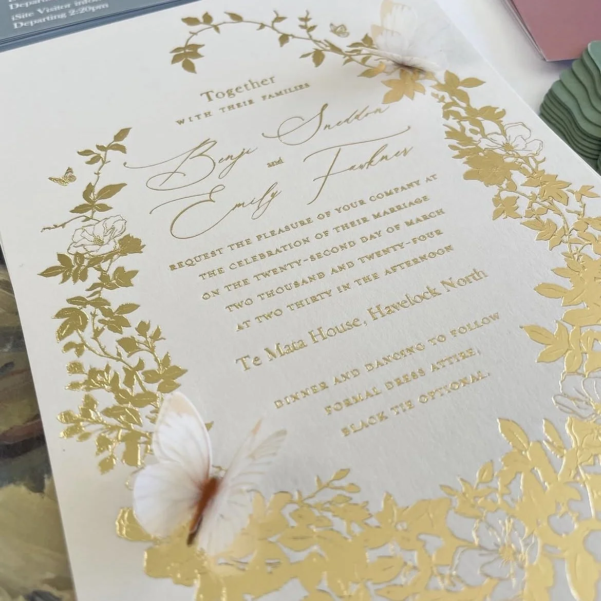 Wedding invitation with gold floral border and elegant cursive text, featuring butterflies and soft pastel accents.