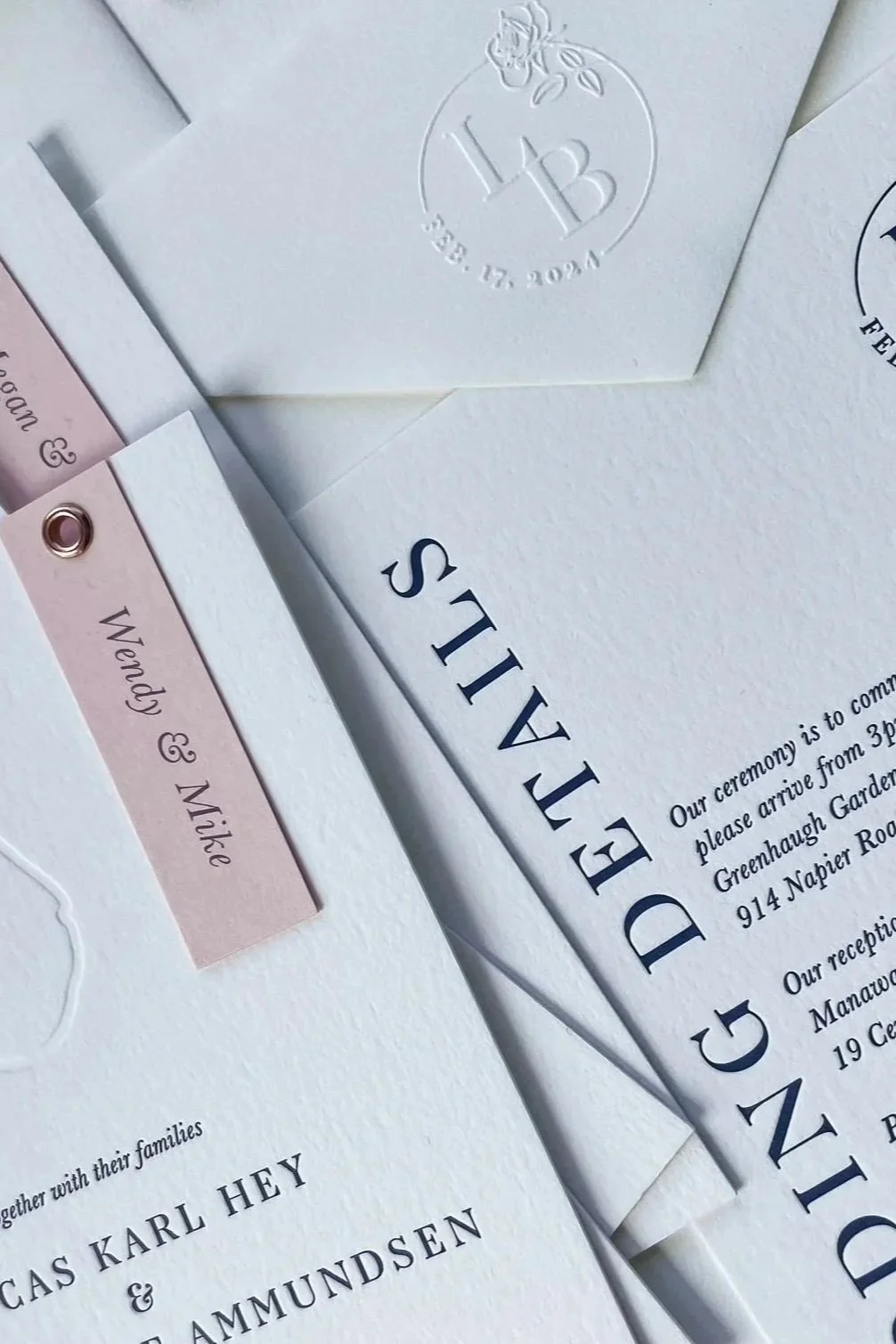 Close-up of wedding invitations and RSVP cards with elegant fonts; includes a white envelope with embossed monogram and floral details.