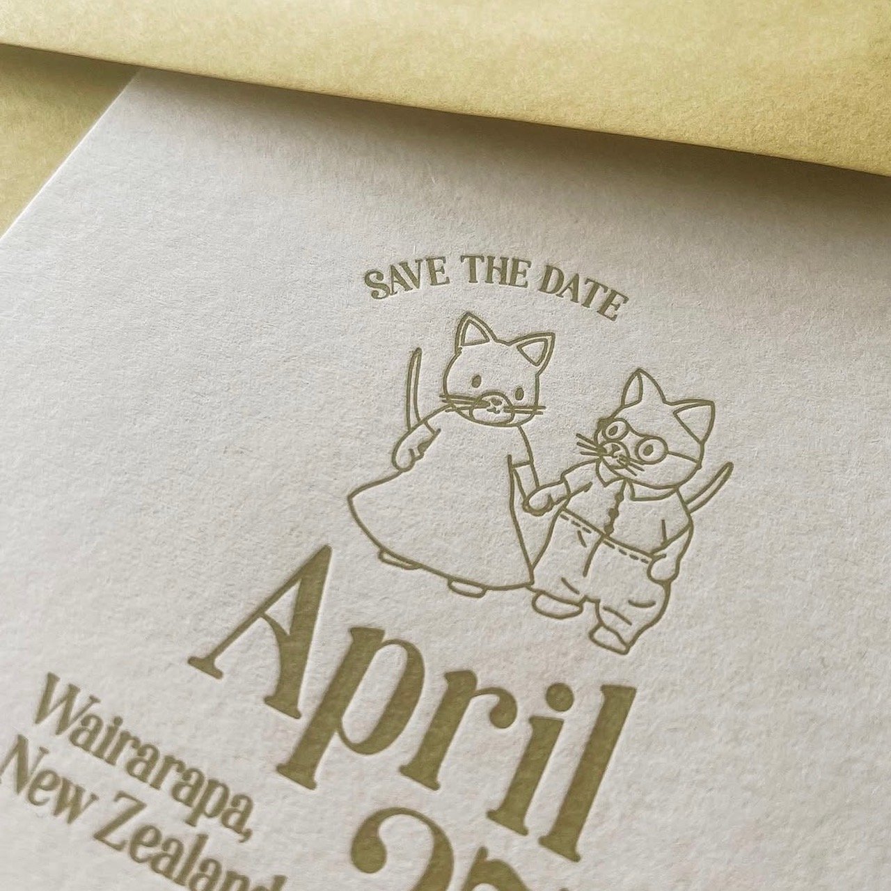 Save the date card featuring a line drawing of two Sylvanian-Family-style cats holding hands, one wearing a dress and the other wearing glasses and pants, with the text "Save the Date" above the cats.