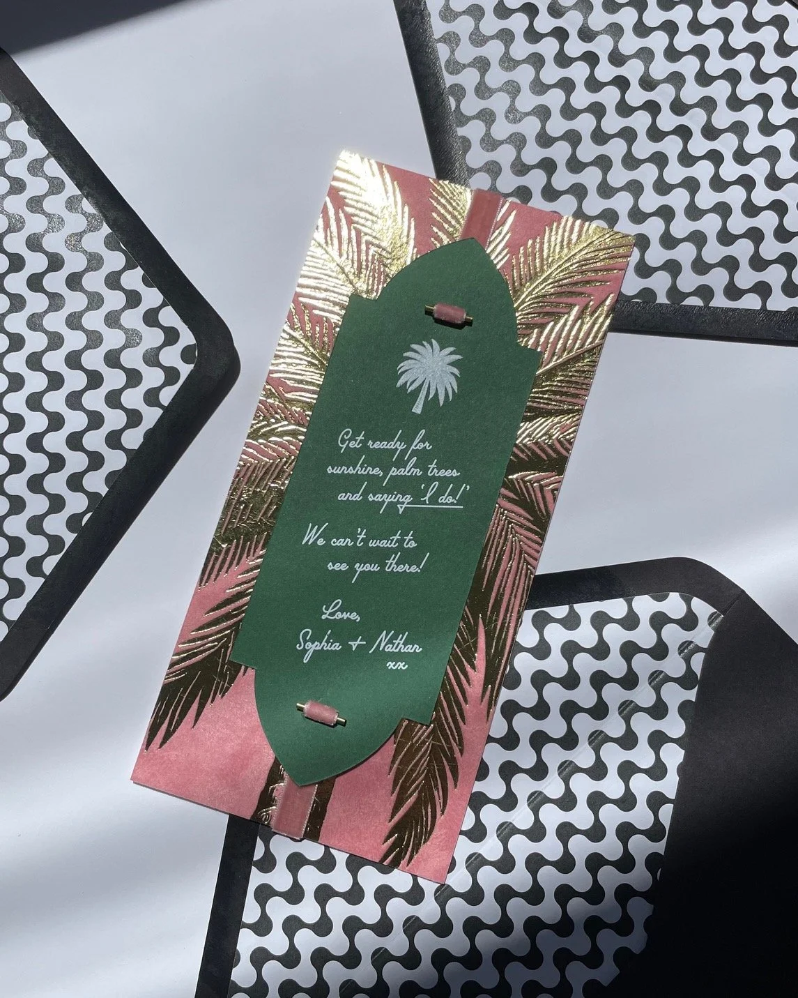 A decorative wedding invitation with a green background and palm leaf design, attached to a pink and gold glittery border. The card contains a message inviting guests to a celebration, signed by Sophia and Nathan.