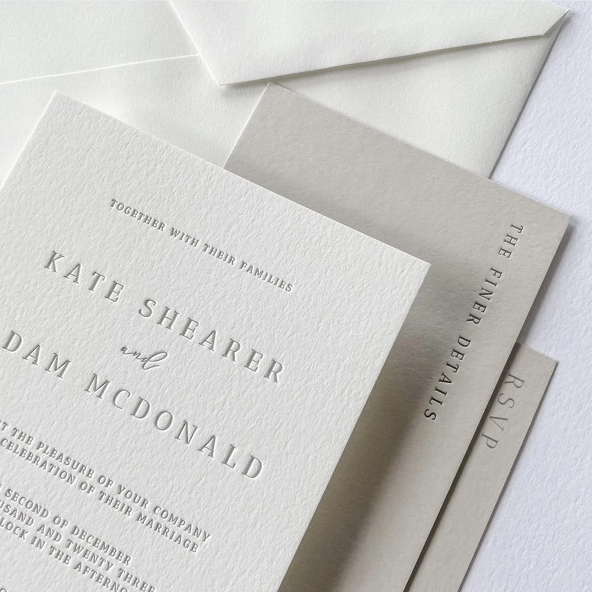 Close-up of elegant wedding invitations with embossed text and matching envelopes in shades of white and gray.
