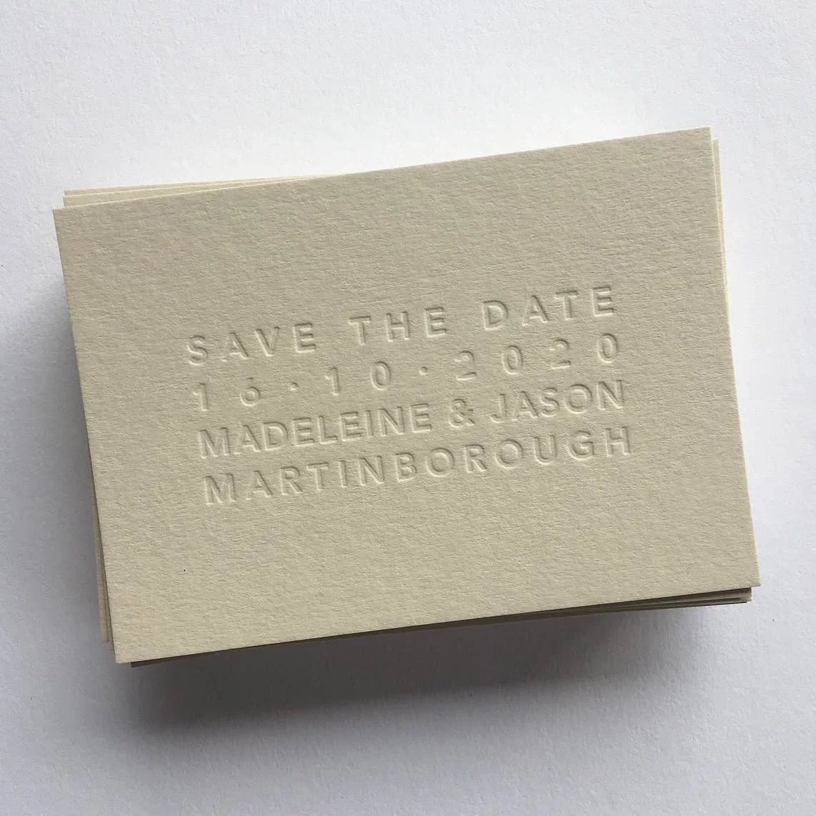 Embossed cream-colored paper with text reading "Save the Date 16.10.2020 Madeline & Jason Martinborough"