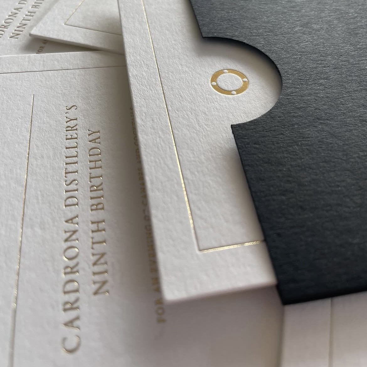 Close-up of wedding stationery with embossed and gold-foiled text, featuring a black and white design with some visible gold accents.