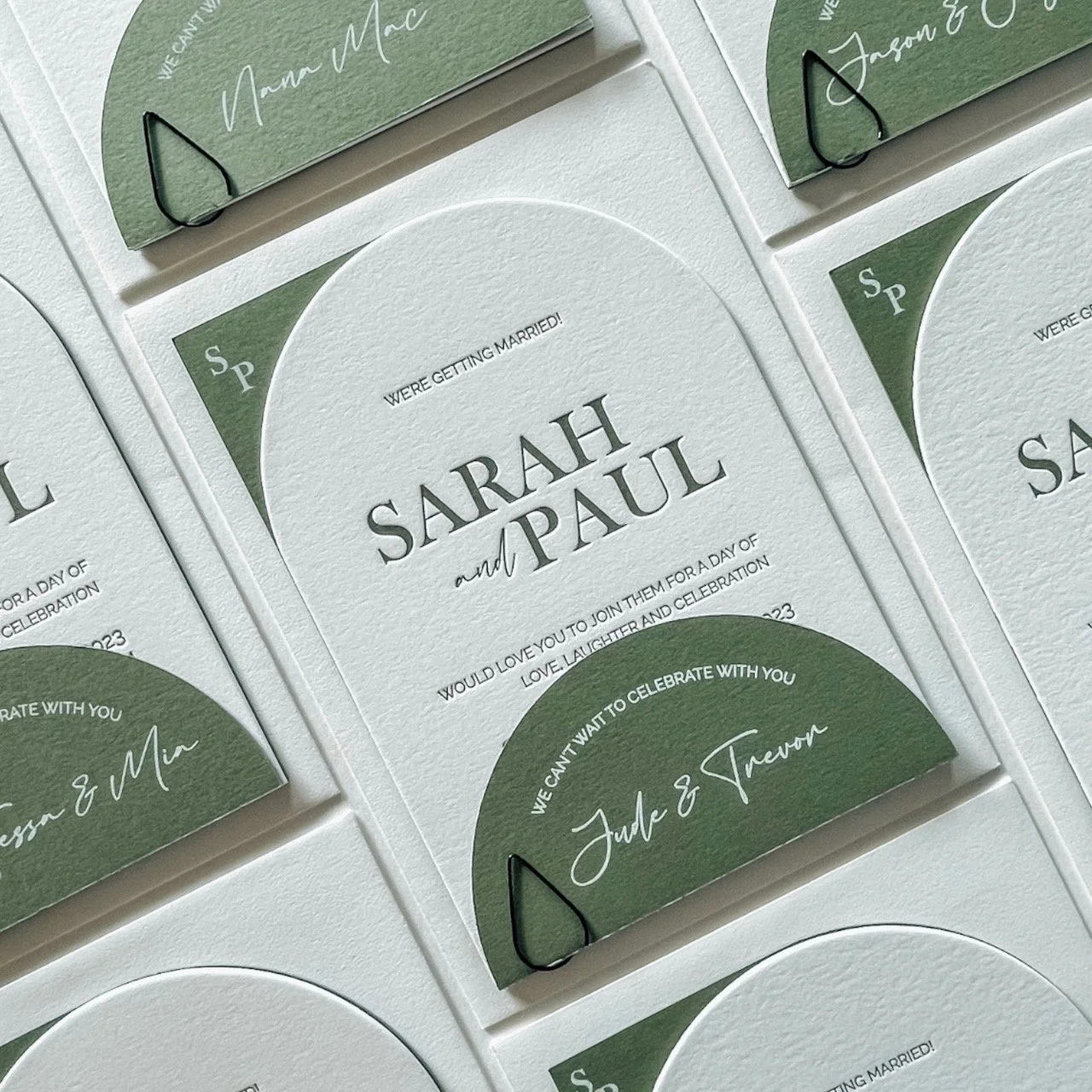 Invitation cards for a wedding with the names Sarah and Paul, featuring a white textured background and green circular accents. The cards include a message about getting married and celebrating love, with decorative black paper clips.