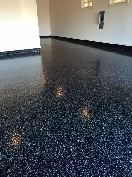 Empty room with a speckled black, white, and gray epoxy floor, white walls, small windows, and some electrical fixtures.