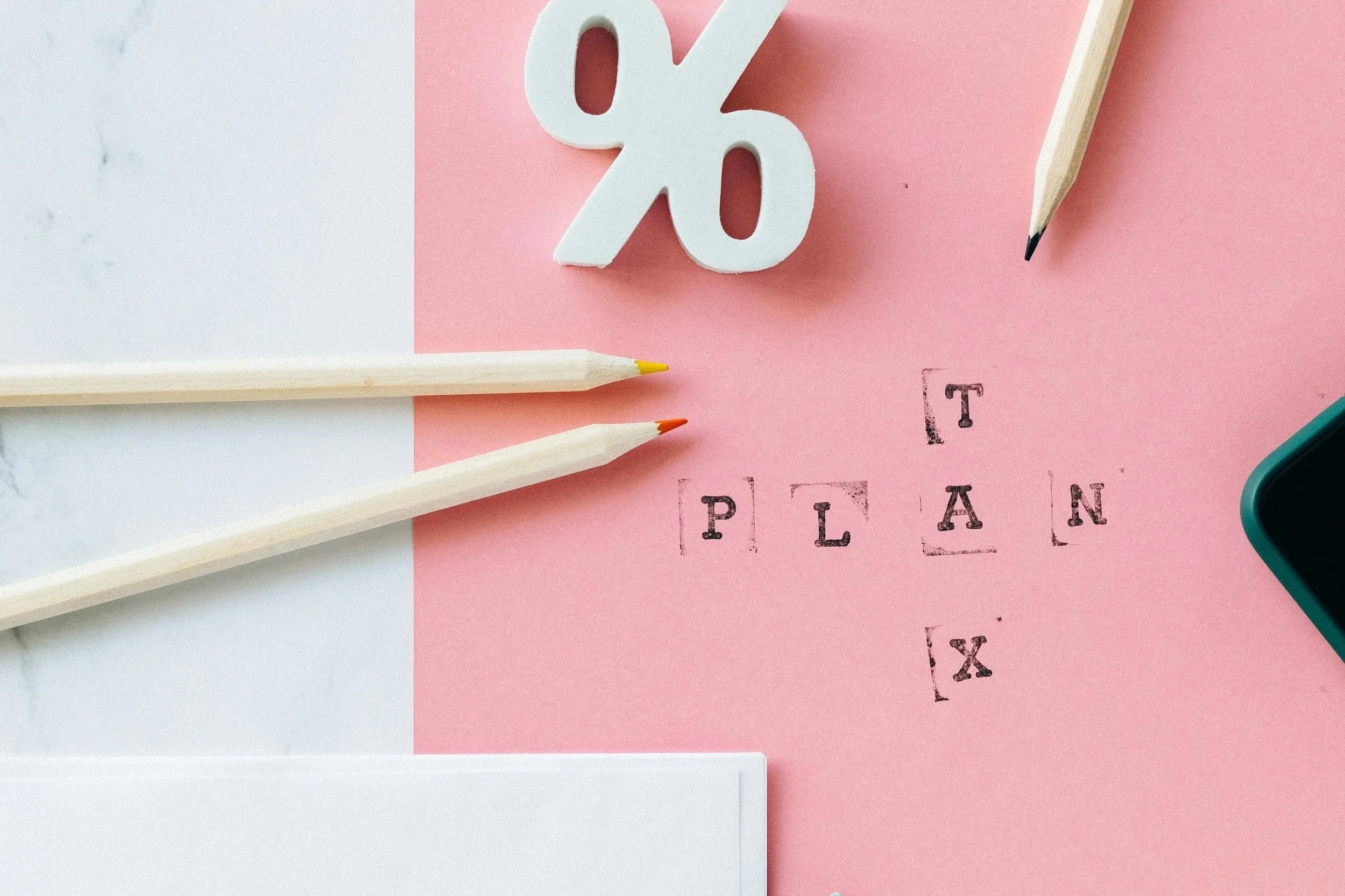 Flat lay of a pink and white background with office supplies and a