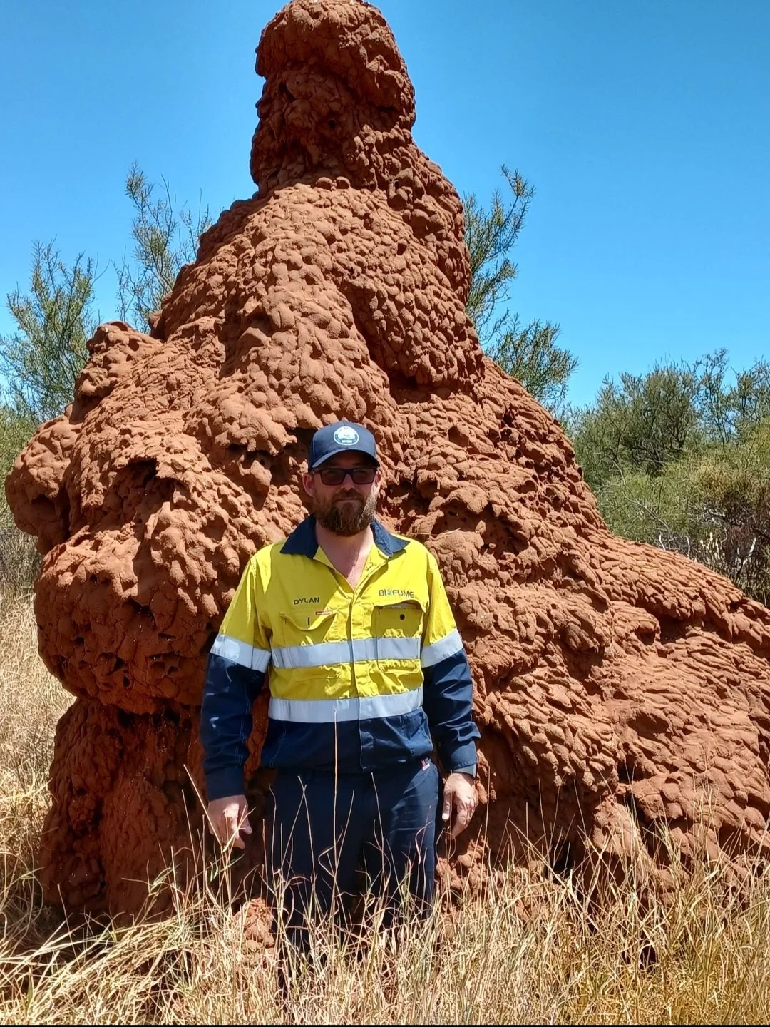Pest technician Dylan from HiveFlow Pest & Weed Management standing beside a large termite mound in Western Australia.
