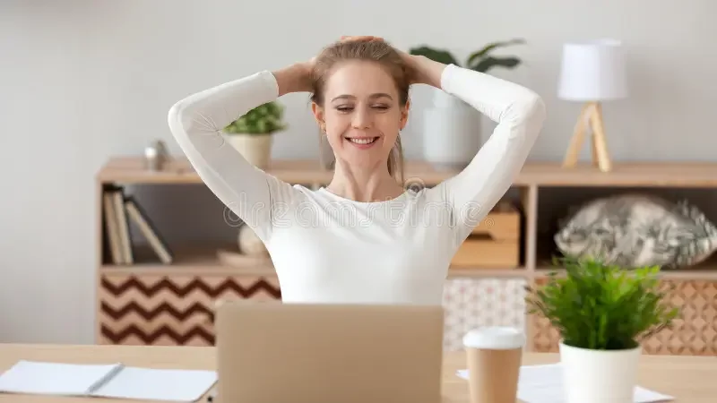 A woman sitting at a desk with a laptop, smiling for completing a task or project