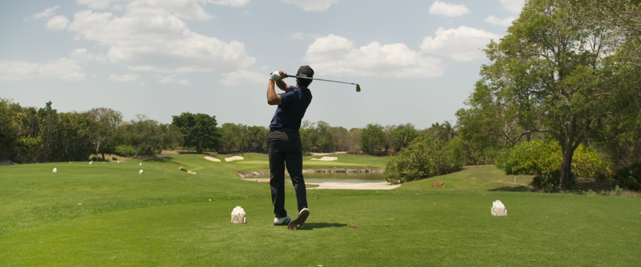 Persona jugando al golf en un campo con árboles y nubes en el cielo.