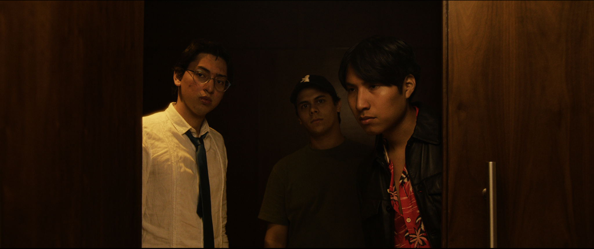 Tres hombres mirando desde un elevador con paredes de madera oscura.