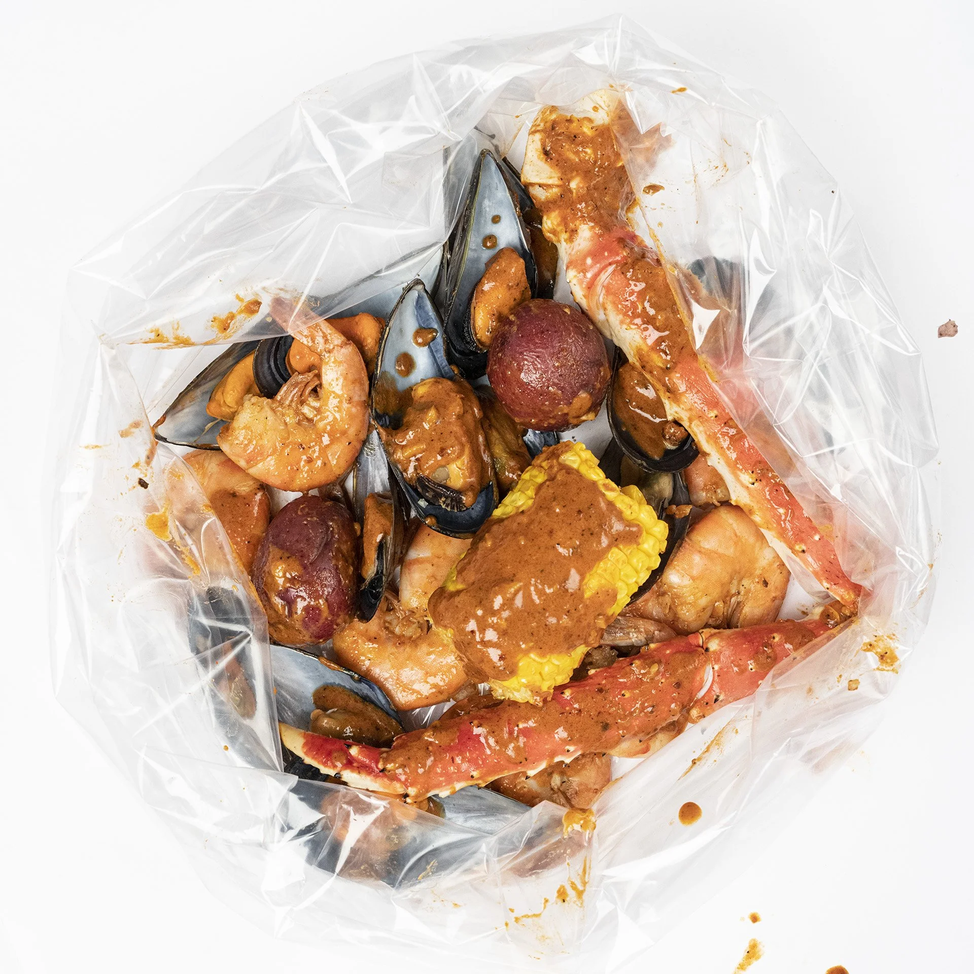 Seafood mixture with shrimp, mussels, crab, vegetables, and sauce in a clear plastic bag.
