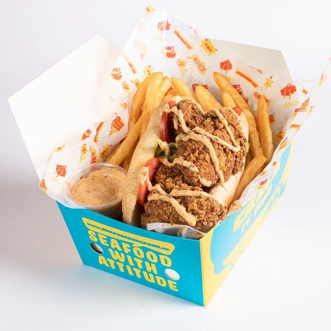 Fried chicken sandwich with fries and dipping sauce in a colorful box.