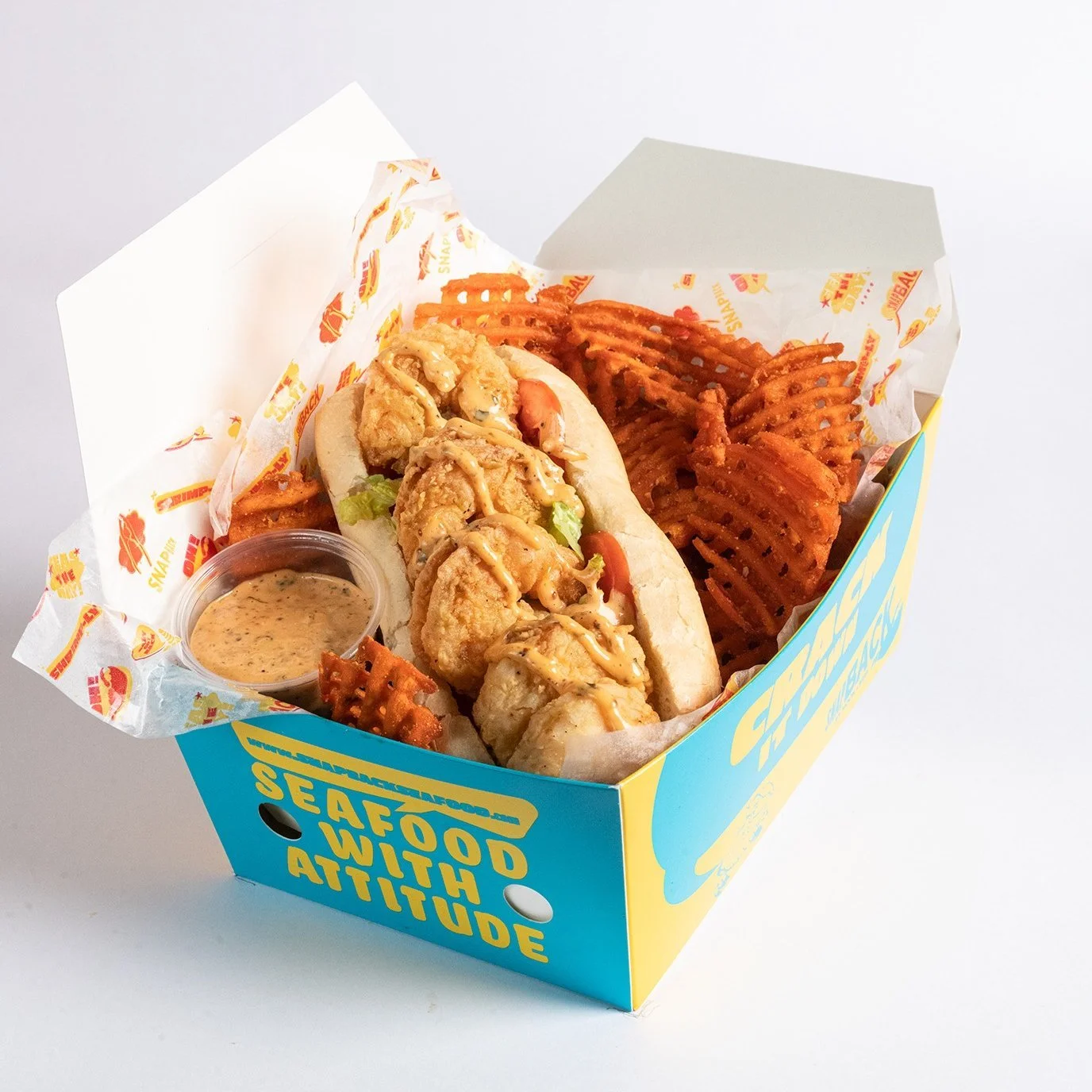 Seafood basket with fried shrimp, waffle fries, dipping sauce, and a fish po' boy sandwich in a blue and yellow seafood restaurant box.