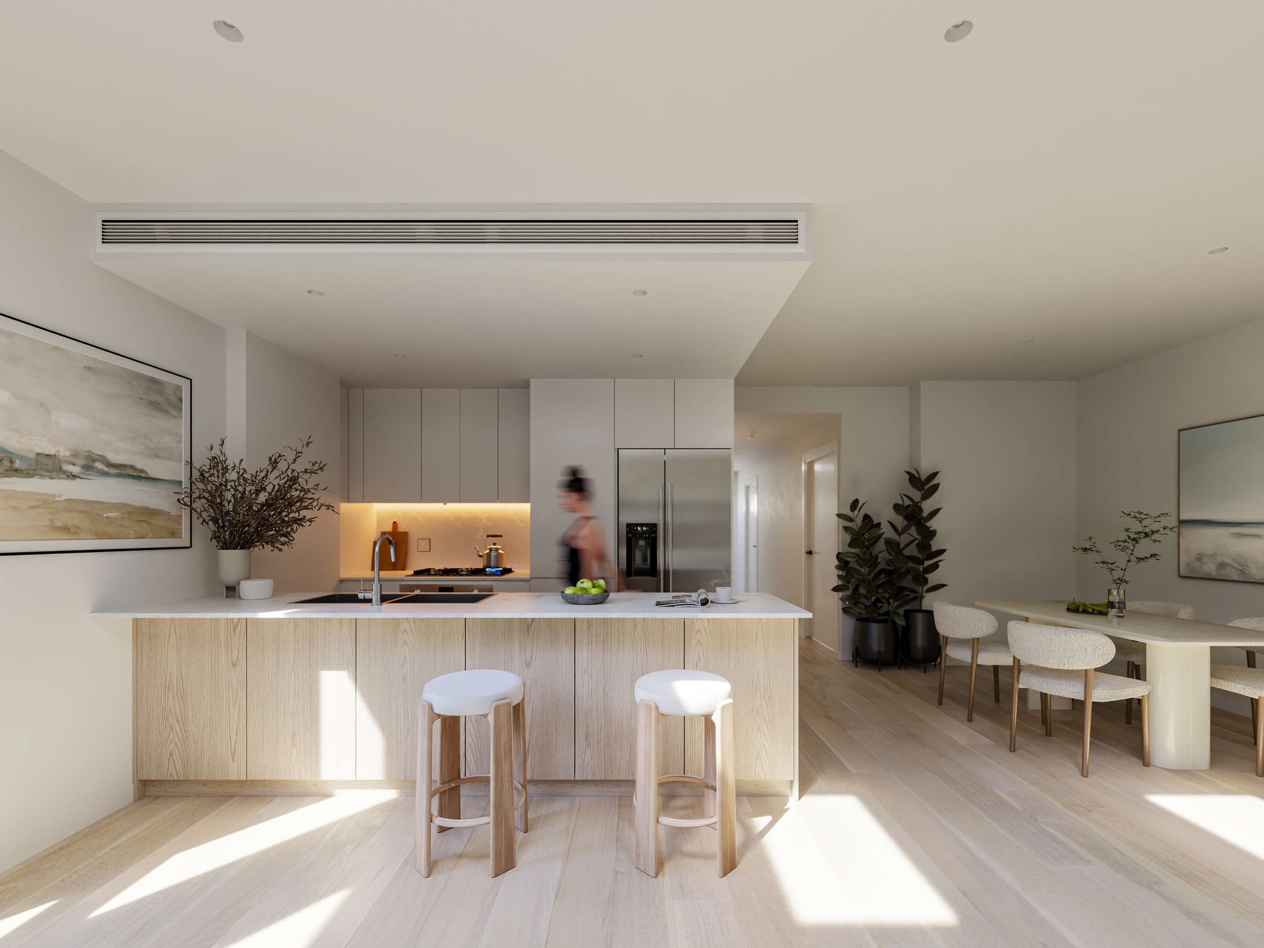 Modern kitchen and dining area with light wood floors, white walls, and minimalist decor. There is a kitchen island with two light wood stools, a potted plant, and a woman walking near the stove. The kitchen has white cabinetry, a stainless steel refrigerator, and a backsplash with under-cabinet lighting. To the right is a dining table with six upholstered chairs and a small potted plant.