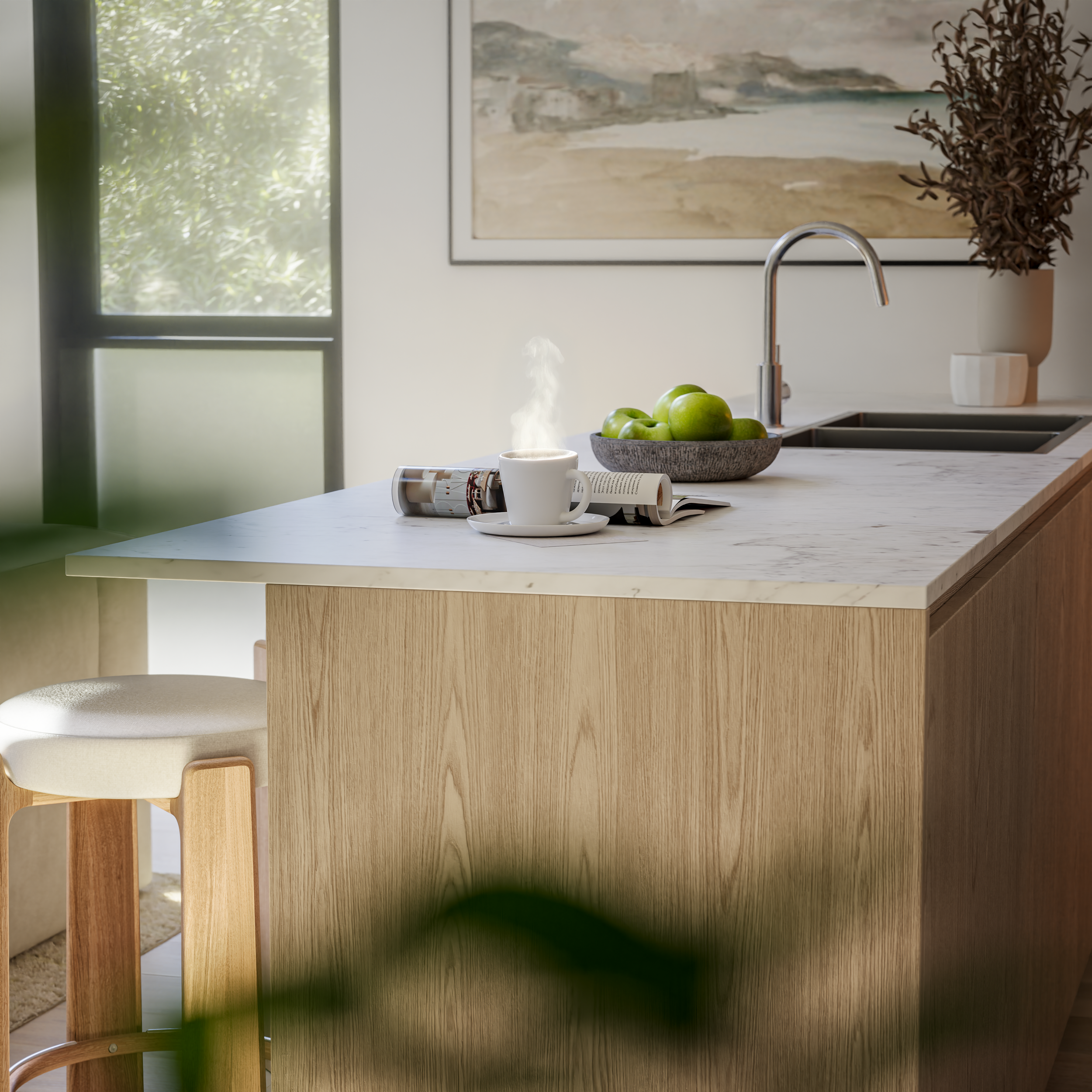Kitchen island with a white marble top, a steaming coffee mug on a saucer, a bowl of green apples, open magazines, a faucet, a window to the left, and a framed painting on the wall.