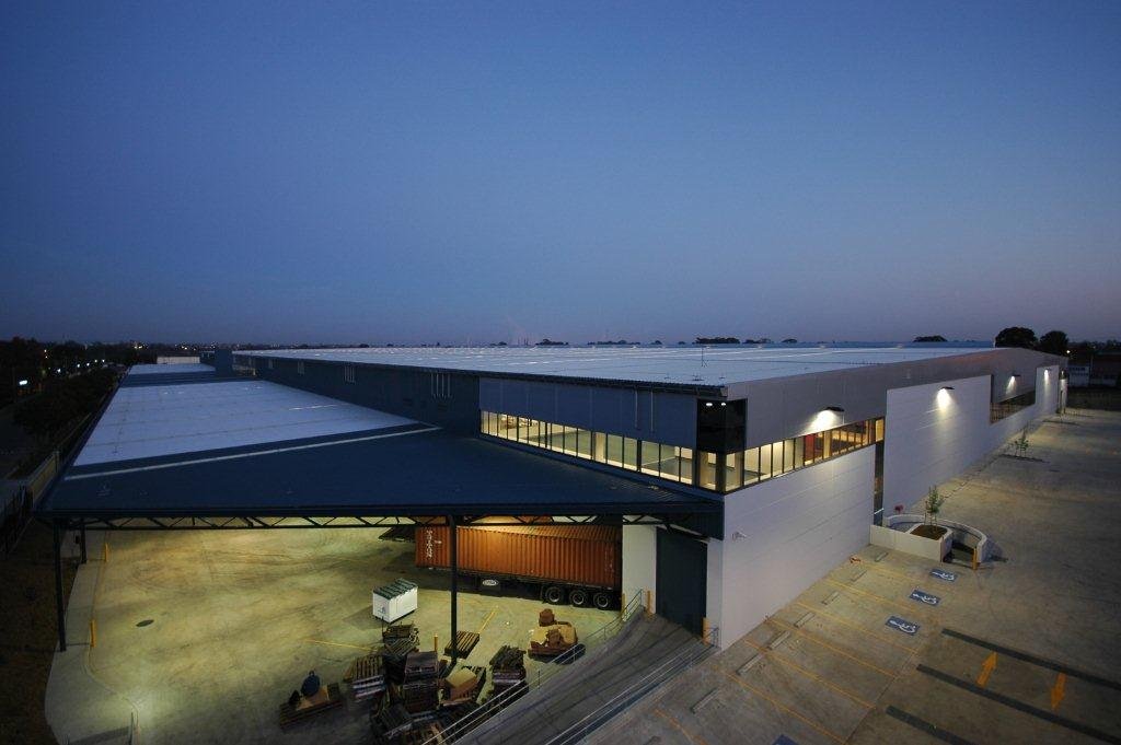 Large warehouse building at dusk with parking lot, shipping container, and outdoor seating area.