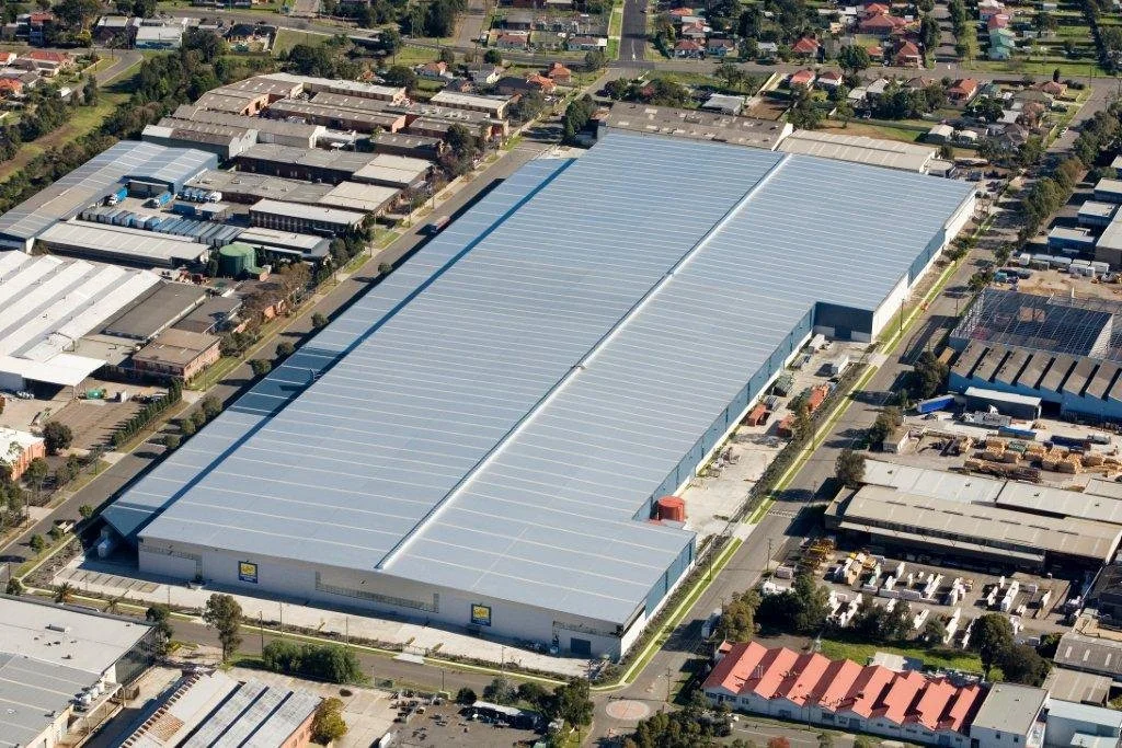 Aerial view of a large industrial warehouse surrounded by roads and neighboring buildings.