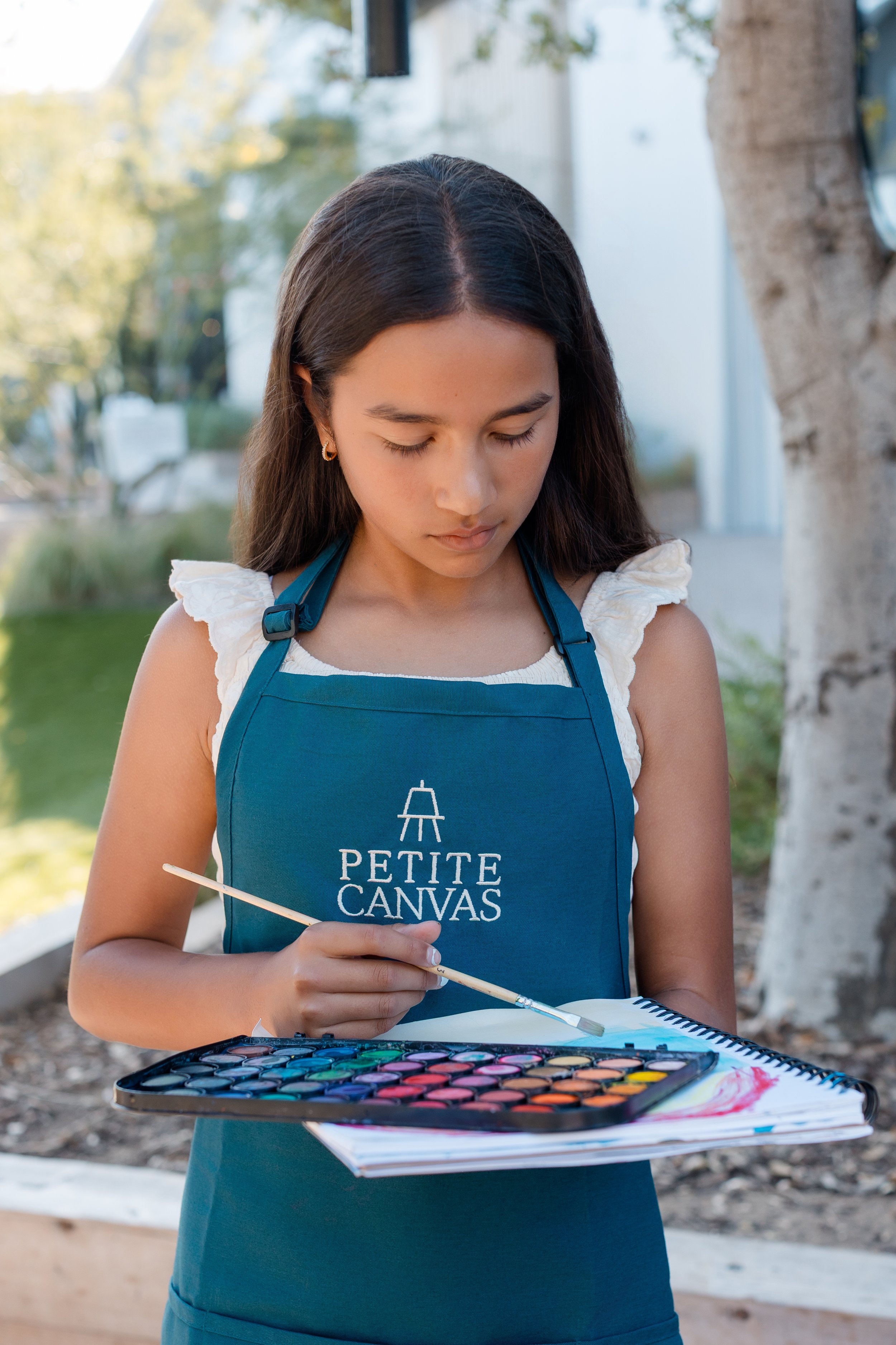 Young artist painting with watercolors while wearing a Petite Canvas apron.
