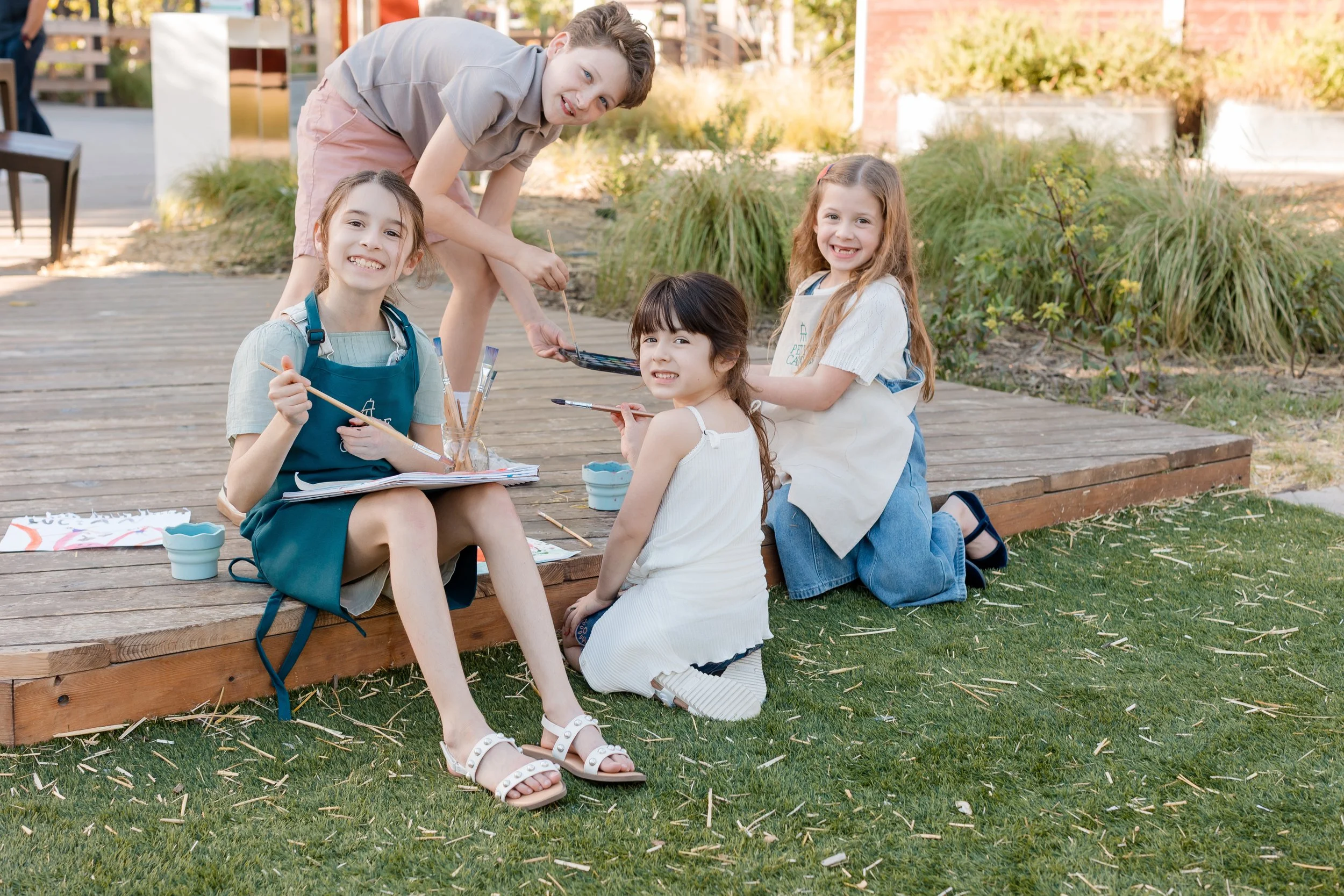 Group of young artists smiling together with paintbrushes and art supplies at Petite Canvas.