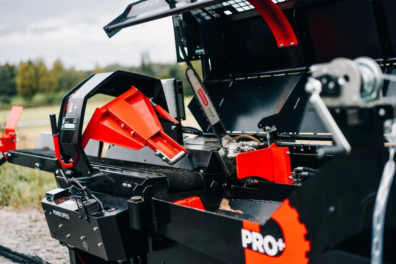 Close-up of a saw cutting through a metal component on a black and red industrial machine outdoors, with blurred natural background.