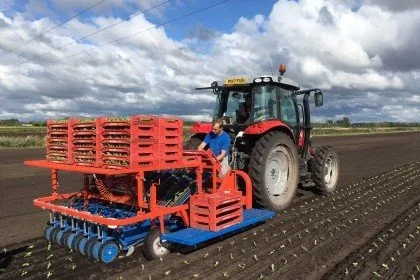 Farmer operating a red tractor with a seed planter attachment in a field under cloudy skies.