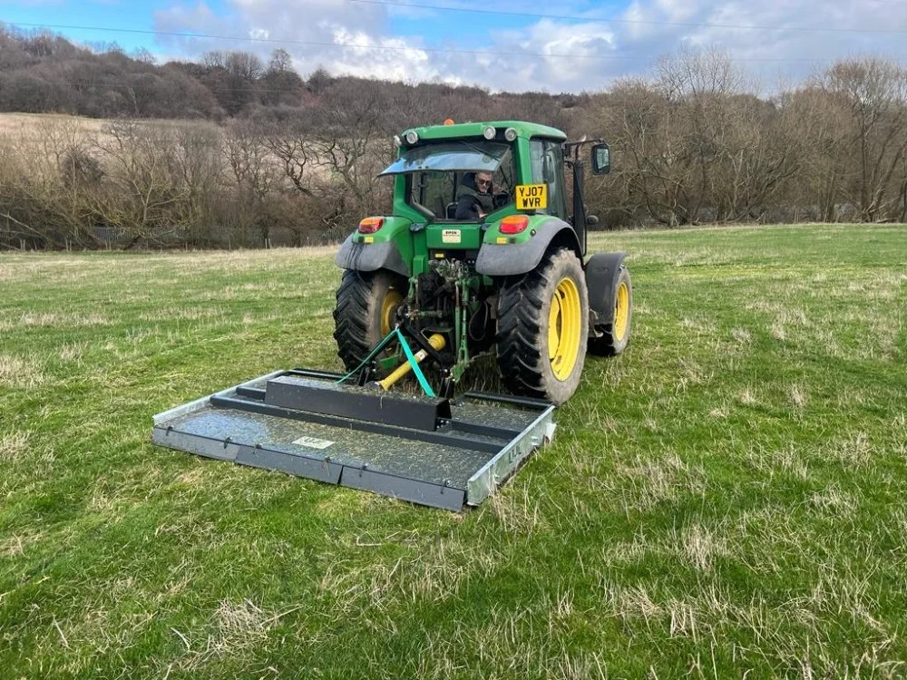 Green tractor with a mower attachment working on a grassy field.
