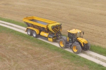 Yellow tractor pulling a large dump trailer along a dirt farm road.