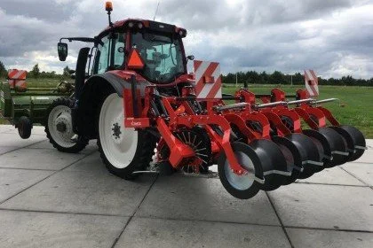 Red tractor with a disc harrow attachment on a concrete surface, overcast sky in the background.